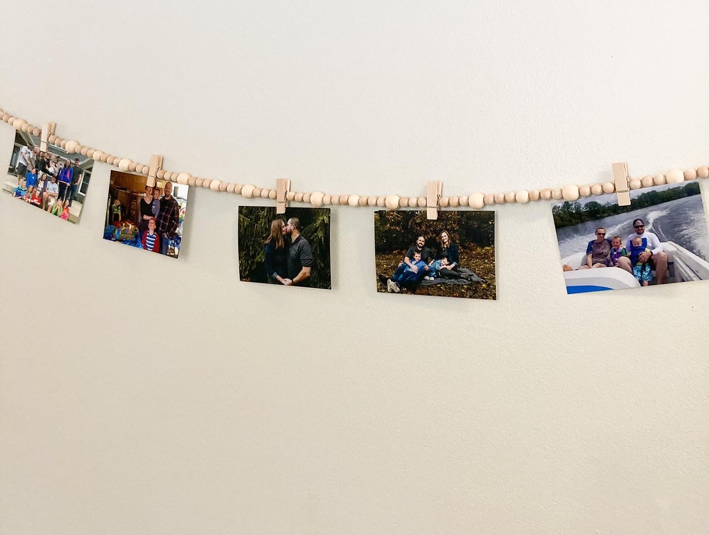 Handmade Wood bead garland display with jute twine tassels and 9 mini clothespins 6.5" total length hanging on wall displaying photographs