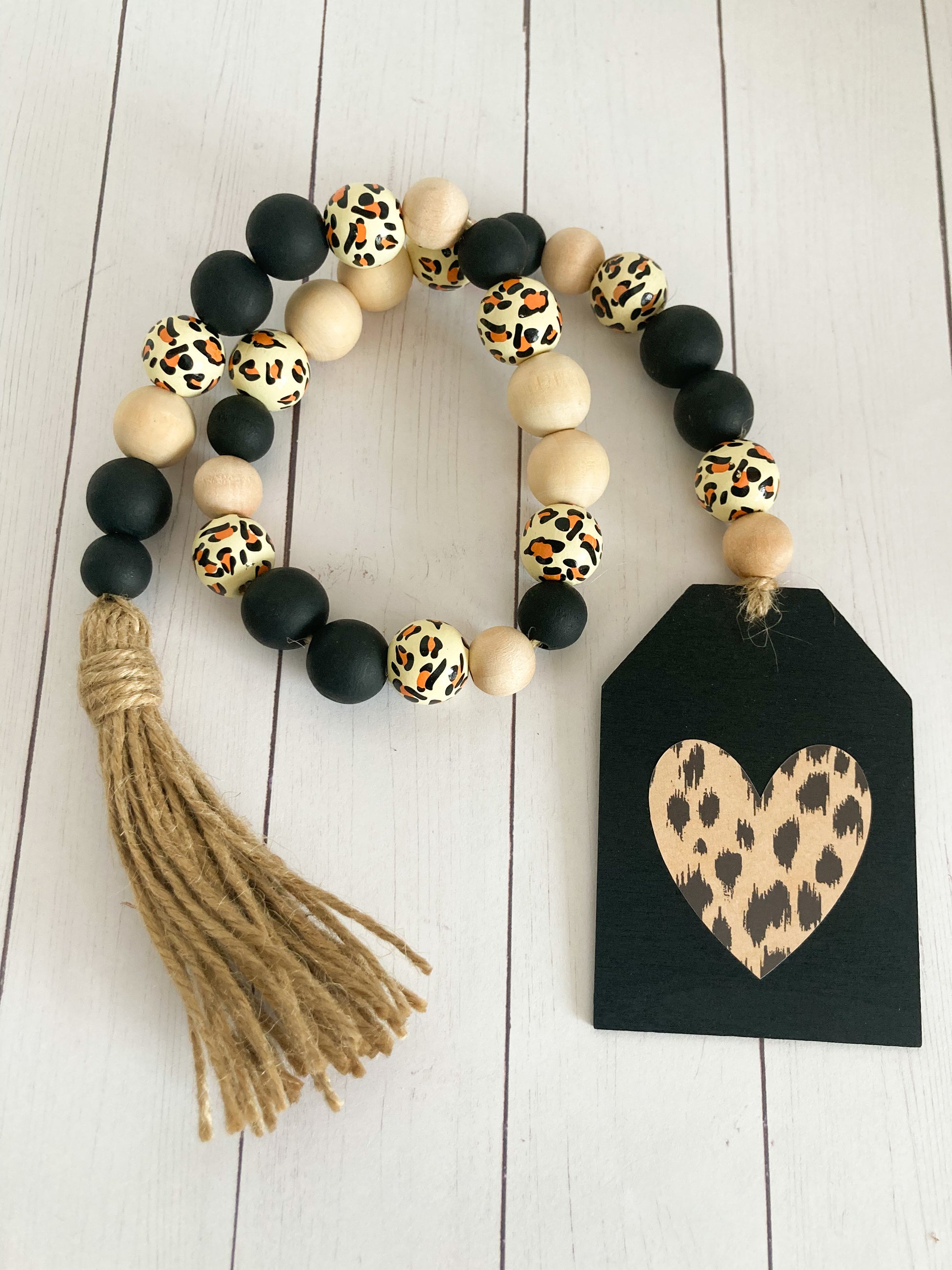Leopard print wood bead garland with a variety of black natural and leopard printed beads jute twine tassel and black painted tag with leopard print heart 24 inches in total length