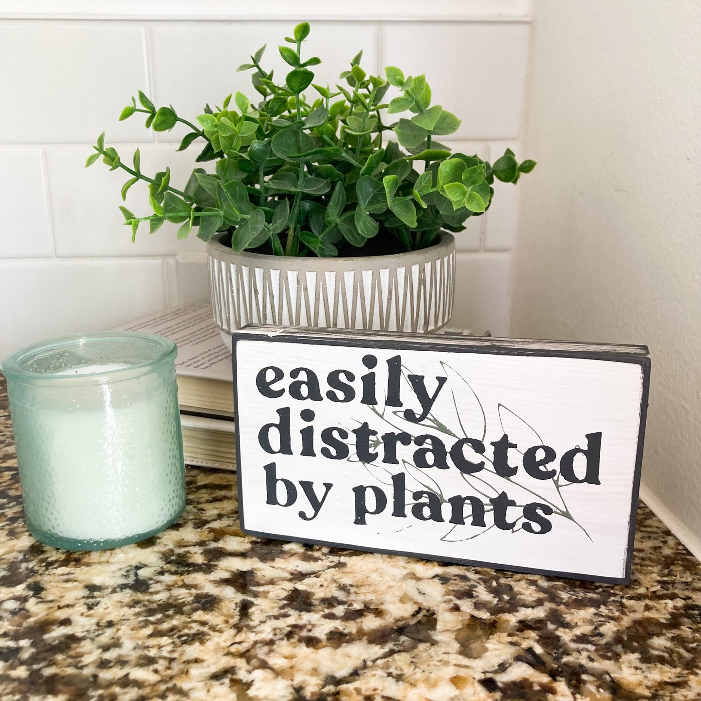 Easily distrated by plants wood sign painted white with black wording and leaf 3.5 inches by 6 inches