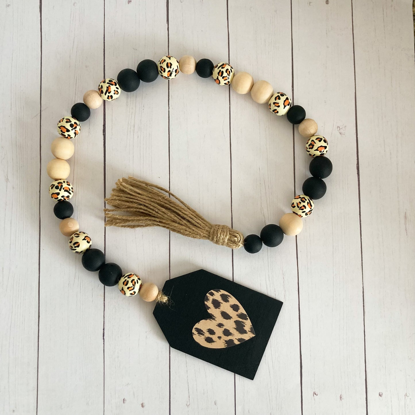 Leopard print wood bead garland with a variety of black natural and leopard printed beads jute twine tassel and black painted tag with leopard print heart 24 inches in total length