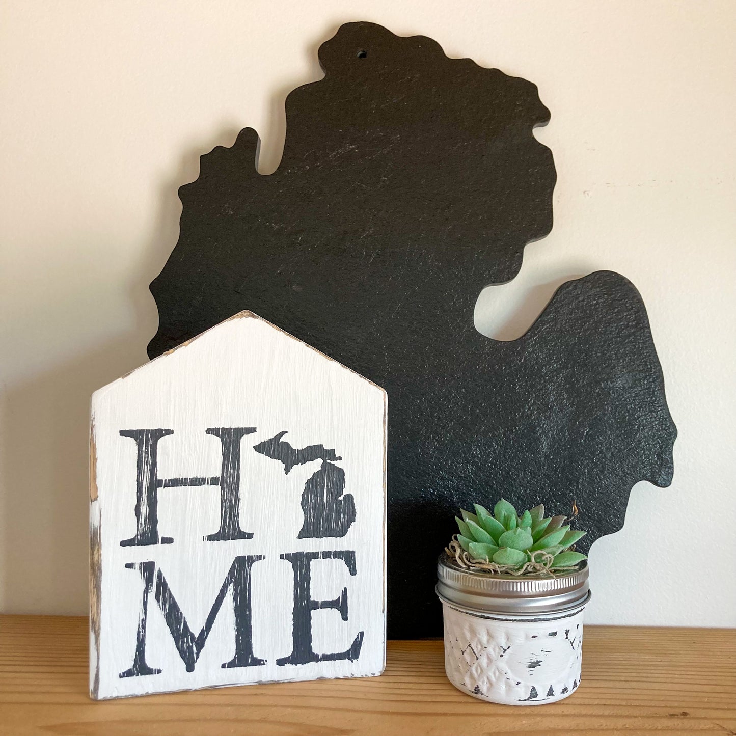 Handmade wood shaped distressed house painted white displaying word home with state of Michigan as the o painted in black approximatly 7 inches by 5 inches by 1.5 inches thick free standing shelf sitter