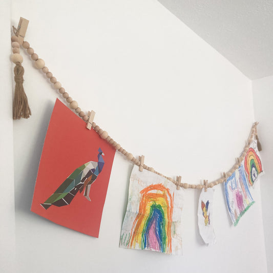 Handmade Wood bead garland display with jute twine tassels and 9 mini clothespins 6.5" total length hanging on wall displaying children's artwork