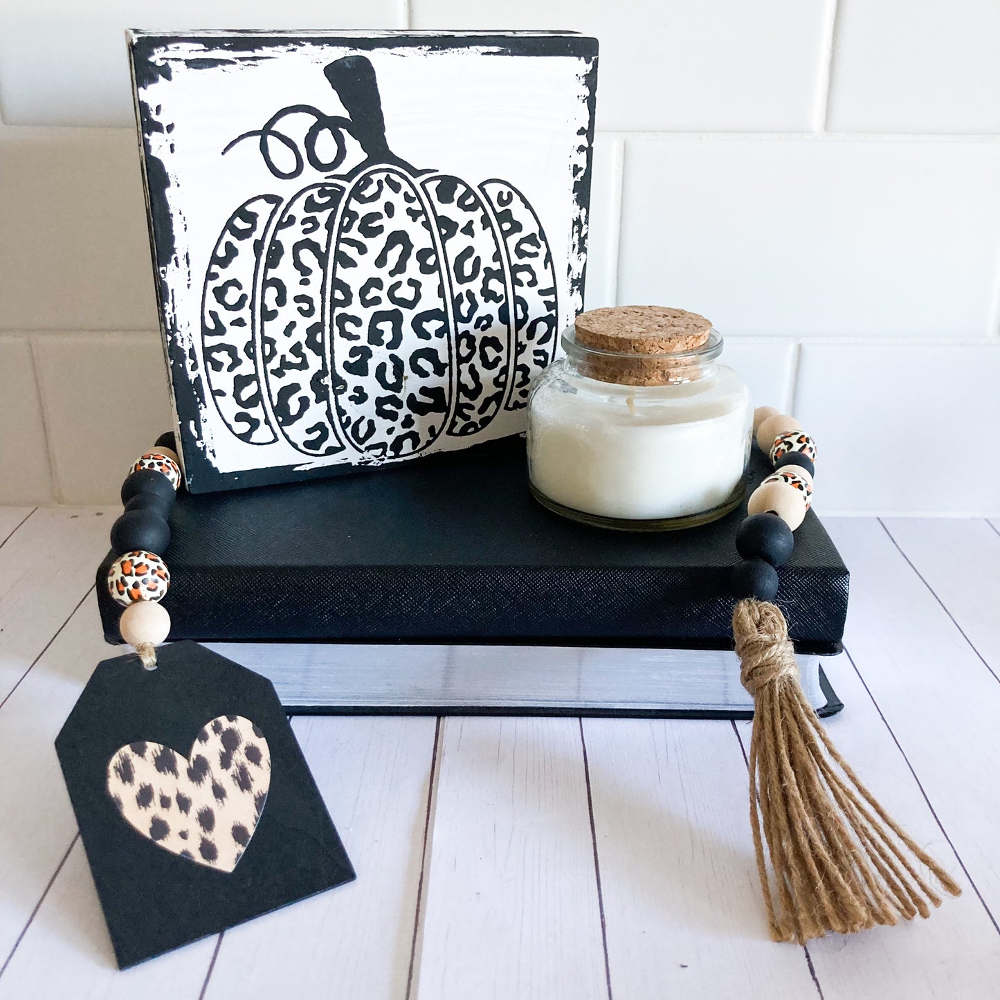 Leopard print wood bead garland with a variety of black natural and leopard printed beads jute twine tassel and black painted tag with leopard print heart 24 inches in total length displayed on a pile of books with a wood sign and candle